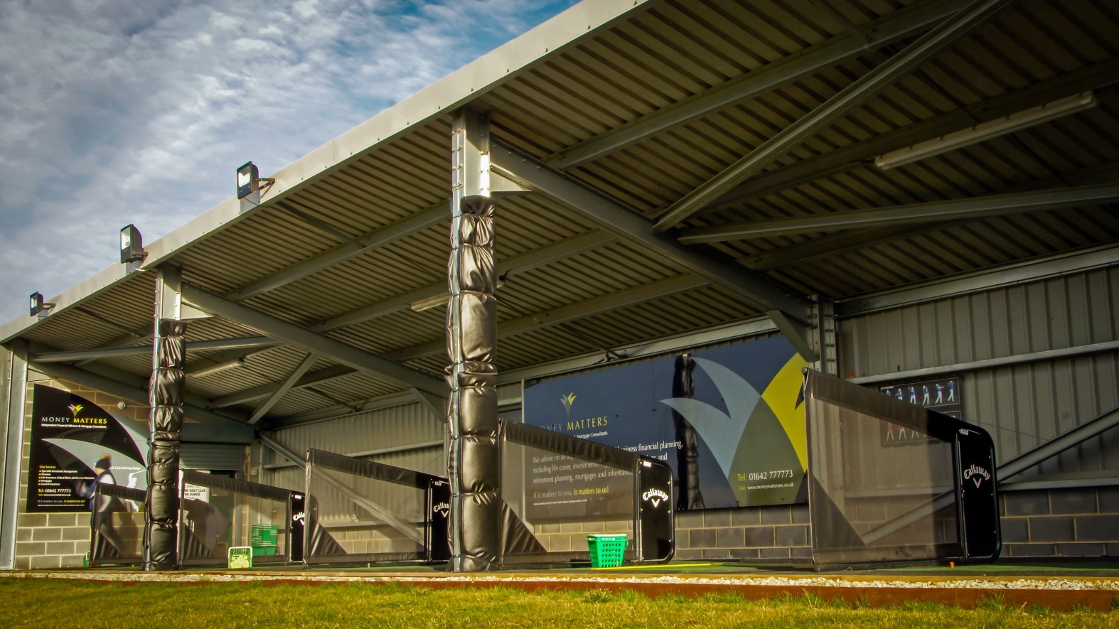 The covered driving range at Cleveland Golf Club seen from the practice area, with the steel roof and bays beneath
